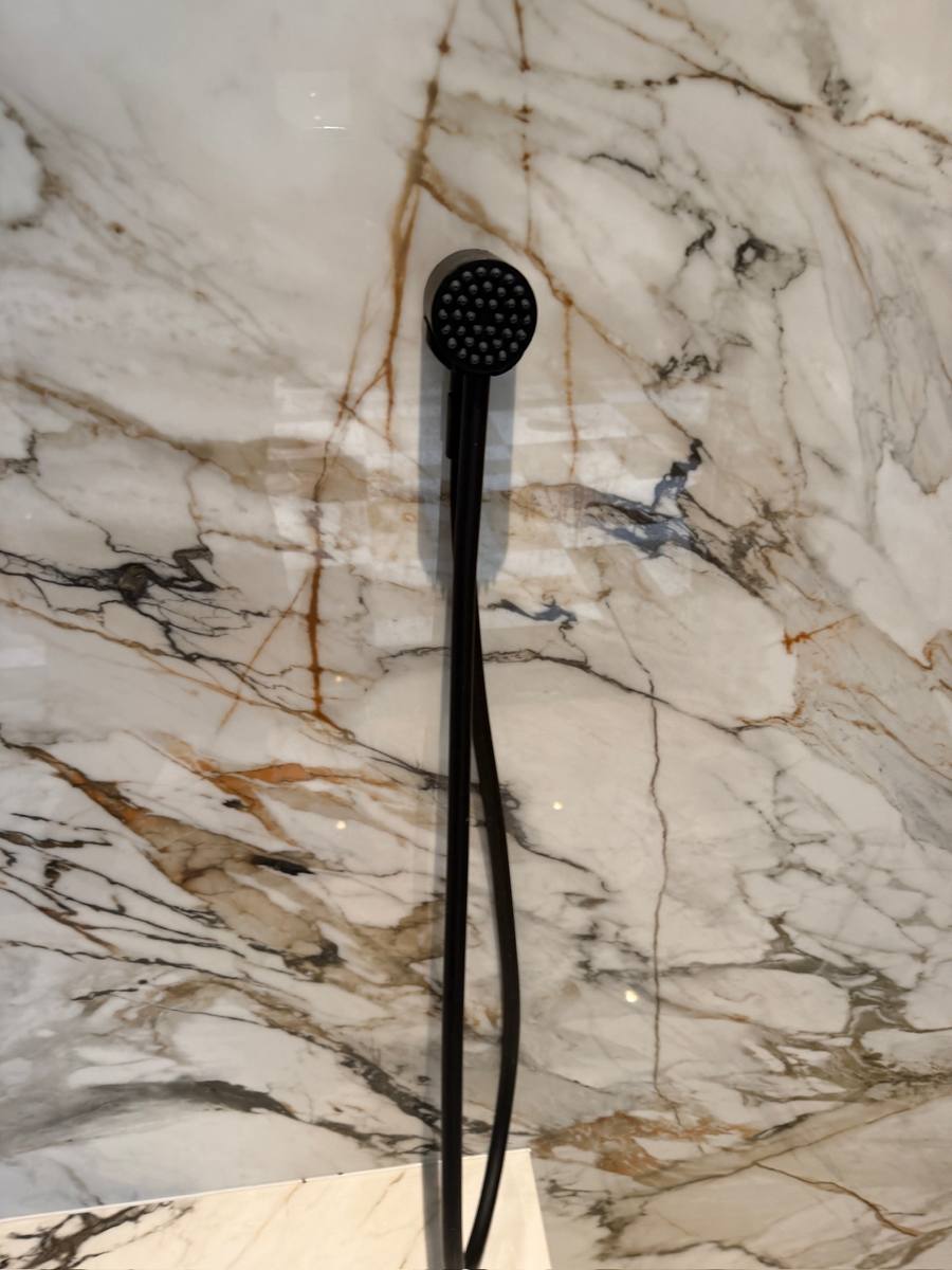 Matte black handheld shower fixture on a marble shower wall in Palm City, FL
